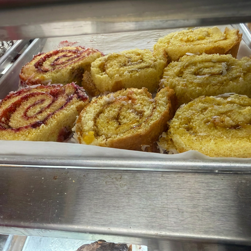Tray of coconut-dusted swiss rolls — strawberry jelly, pineapple, and cinnamon swirl slices.