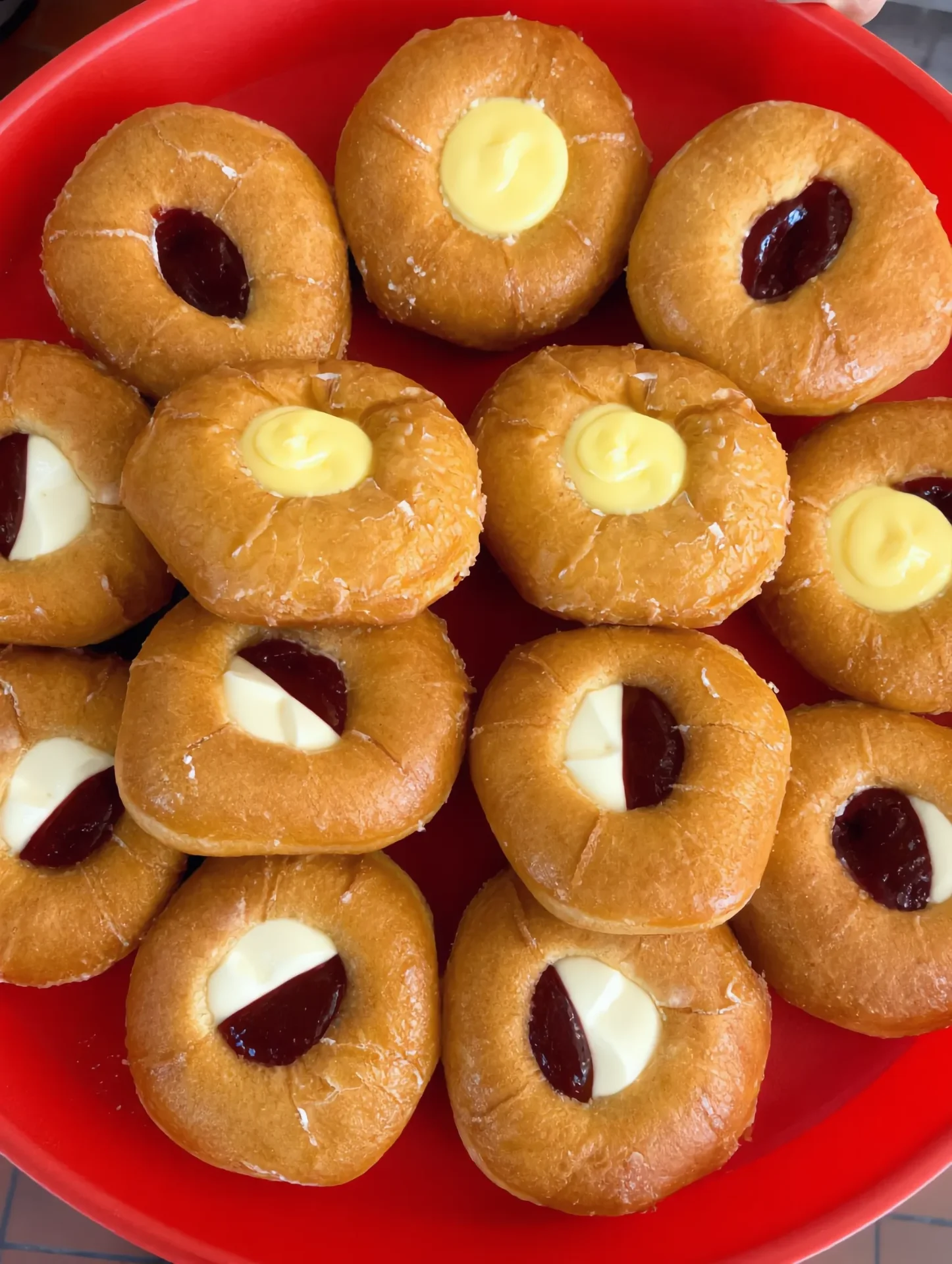 A red tray piled with filled donuts — strawberry jelly, Bavarian cream, lemon, and cream-and-jelly combos, glaze still fresh.