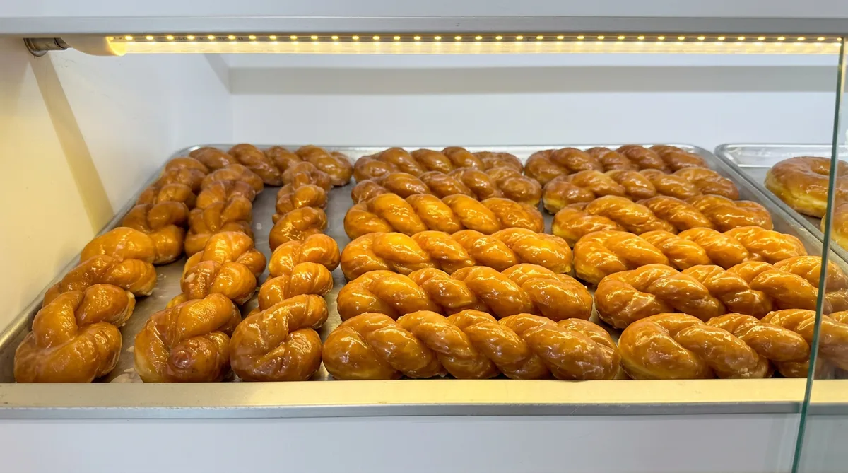 Glazed braided twist donuts packed tight in the display case under warm light.